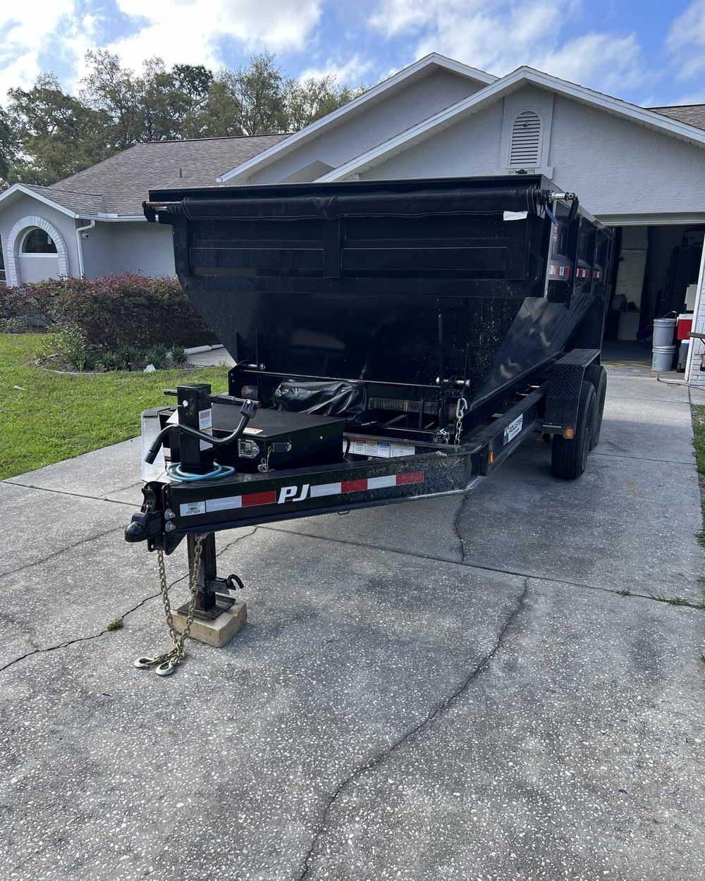 The Dump It trailer with a container on it, backed into a driveway at a house